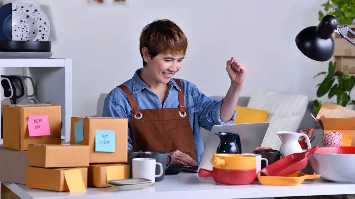 Imagem que ilustra como transformar um pequeno negócio em uma marca forte, com uma empreendedora sorrindo e interagindo com um computador, cercada por utensílios e caixas de embalagem.
