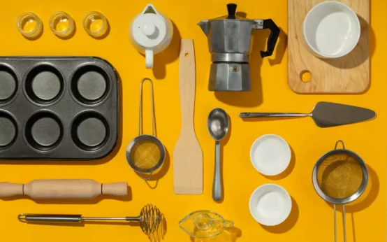 Variedades de utensílios essenciais para cozinhas modernas, incluindo formas para assar, colheres, espátulas, peneiras, e utensílios de medição, organizados sobre fundo amarelo.