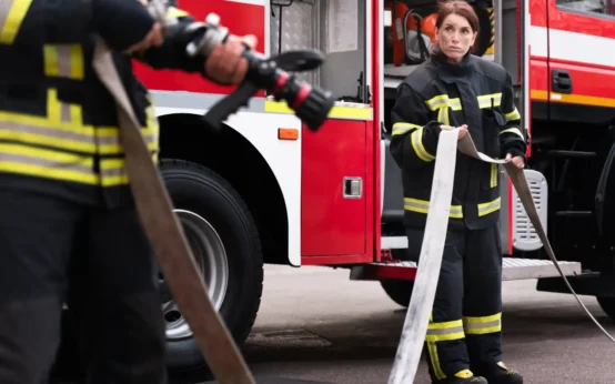 Duas bombeiras treinando com mangueira de incêndio ao lado de um caminhão de combate a incêndios, destacando a importância do curso de brigada de incêndio mesmo sem atuar na área.