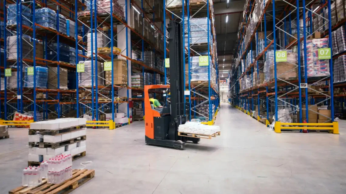 Imagem de um armazém de grande porte com empilhadeiras movimentando mercadorias e pallets, representando tendências e atualizações no mercado de empilhadeiras no Brasil.