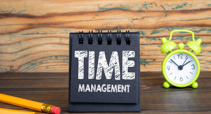 Bloco de notas com a frase “Time Management” ao lado de relógio verde sobre mesa de madeira.
