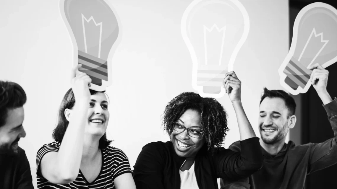 Grupo de pessoas comemorando e segurando lâmpadas de papel que representam inovação e criatividade em modelos de negócios inovadores