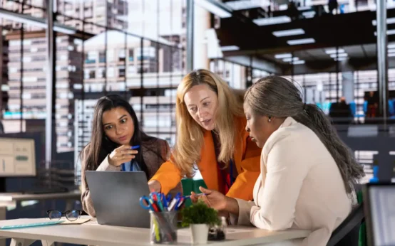 Três profissionais de empresas diferentes colaborando em uma reunião no escritório moderno, discutindo estratégias para desenvolver uma cultura de inovação empresarial.