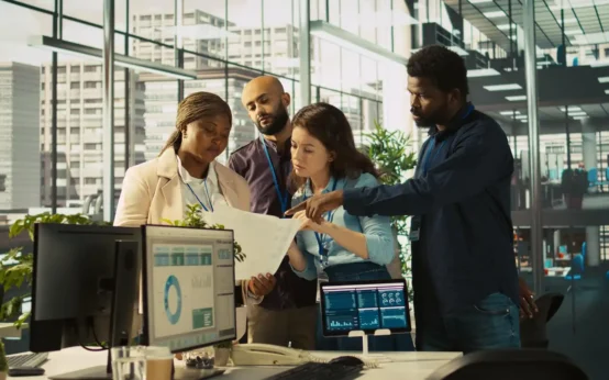 Profissionais de diferentes origens colaborando em um ambiente de escritório moderno com tecnologia avançada, promovendo inovação aberta por meio de parceria entre empresas e startups.