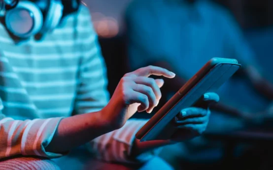 Mãos utilizando um tablet em um ambiente com iluminação azul, sugerindo Principais Tendências De Tecnologia Que Devem Ganhar Espaço Nos Próximos Anos e uso de dispositivos digitais