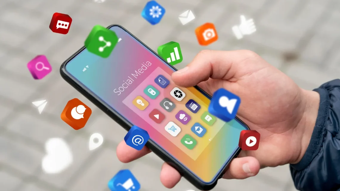 Mão segurando um celular com ícones de redes sociais na tela e notificações de consumo de notícias, simbolizando Redes Sociais e consumo de notícias: Como mudou a forma de acompanhar acontecimentos