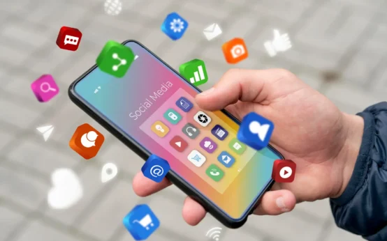 Mão segurando um celular com ícones de redes sociais na tela e notificações de consumo de notícias, simbolizando Redes Sociais e consumo de notícias: Como mudou a forma de acompanhar acontecimentos